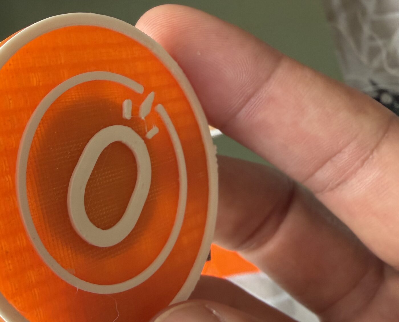 A clay-orange Block Coin held between finger and thumb, showing its raised white emblem.